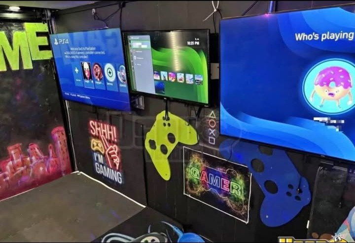 Inside the Wofford gaming trailer: three HD TVs mounted on the wall running PlayStation, with neon gaming signs